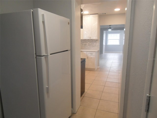 kitchen featuring ceiling fan, light tile patterned flooring, white refrigerator, decorative backsplash, and white cabinets