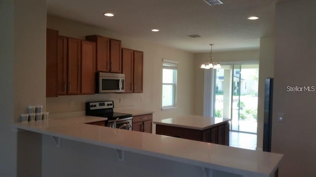 kitchen featuring a breakfast bar, hanging light fixtures, appliances with stainless steel finishes, a notable chandelier, and kitchen peninsula