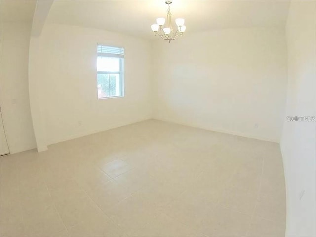 tiled spare room featuring a notable chandelier