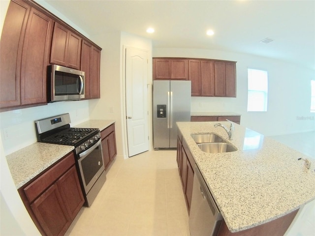 kitchen featuring a kitchen island with sink, sink, light stone counters, and appliances with stainless steel finishes