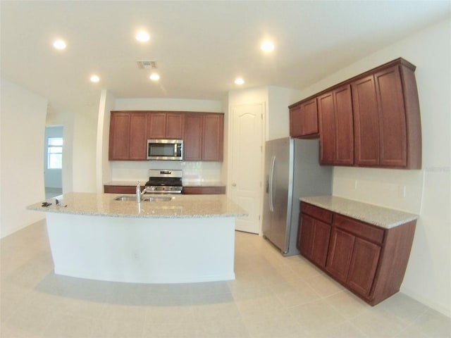 kitchen featuring a kitchen island with sink, sink, light tile patterned floors, appliances with stainless steel finishes, and light stone counters