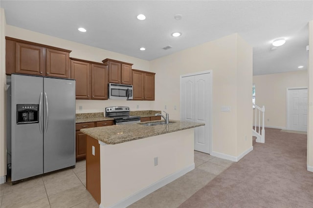 kitchen featuring light carpet, light stone counters, stainless steel appliances, sink, and an island with sink