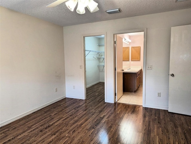 unfurnished bedroom with a walk in closet, dark hardwood / wood-style flooring, a textured ceiling, ceiling fan, and a closet