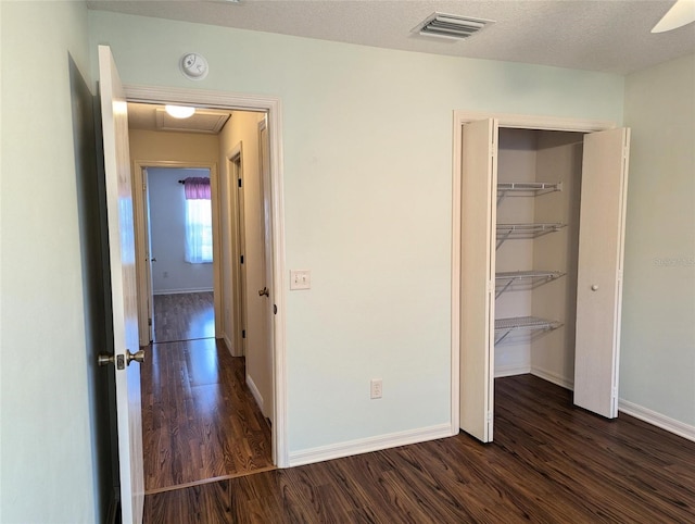 unfurnished bedroom featuring a textured ceiling, dark hardwood / wood-style flooring, a closet, and ceiling fan