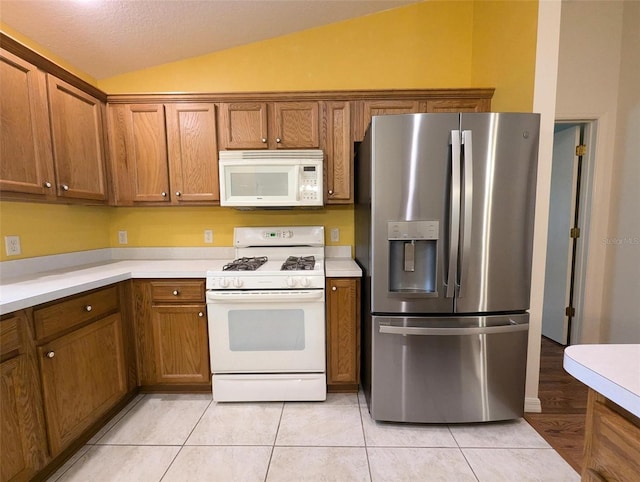 kitchen featuring white appliances, a textured ceiling, light tile patterned floors, and vaulted ceiling