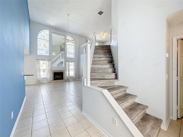 stairs with tile patterned flooring, ceiling fan, a towering ceiling, and a fireplace