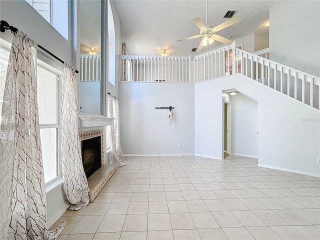 unfurnished living room featuring a tiled fireplace, ceiling fan, light tile patterned floors, and a high ceiling