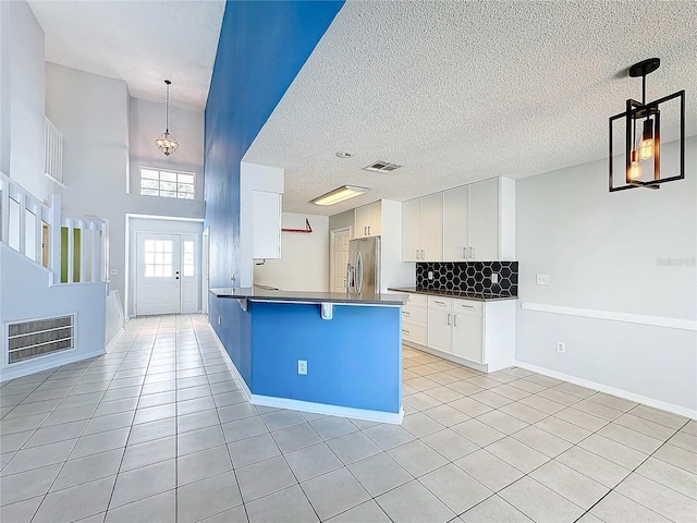 kitchen featuring stainless steel refrigerator, white cabinetry, hanging light fixtures, a kitchen bar, and light tile patterned floors