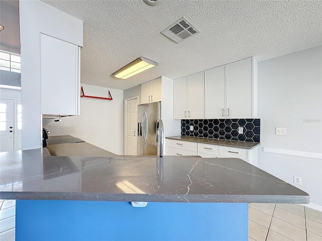 kitchen with kitchen peninsula, stainless steel refrigerator with ice dispenser, a textured ceiling, white cabinetry, and light tile patterned flooring