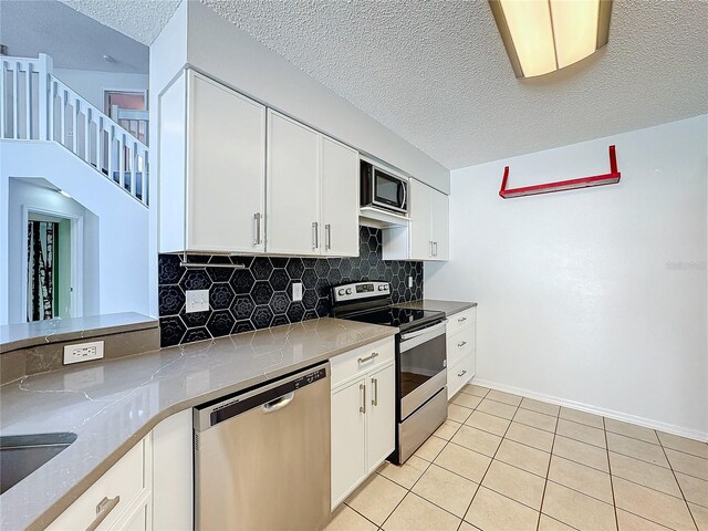 kitchen featuring white cabinets, a textured ceiling, tasteful backsplash, light tile patterned flooring, and stainless steel appliances