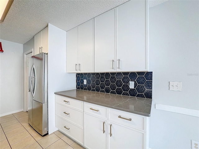 kitchen with backsplash, white cabinets, a textured ceiling, light tile patterned flooring, and stainless steel refrigerator