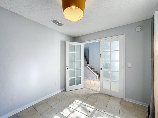 tiled spare room with a textured ceiling and french doors