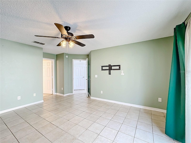 spare room featuring ceiling fan, light tile patterned floors, and a textured ceiling