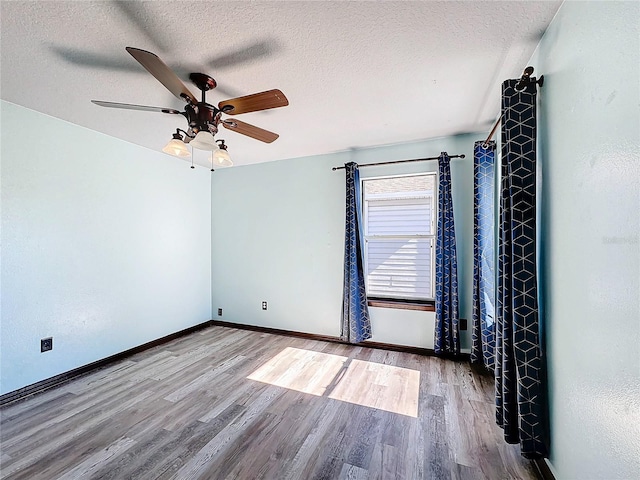 empty room with ceiling fan, wood-type flooring, and a textured ceiling