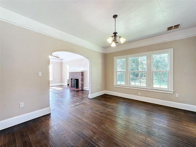 unfurnished living room featuring ornamental molding, a brick fireplace, dark wood-type flooring, and a notable chandelier