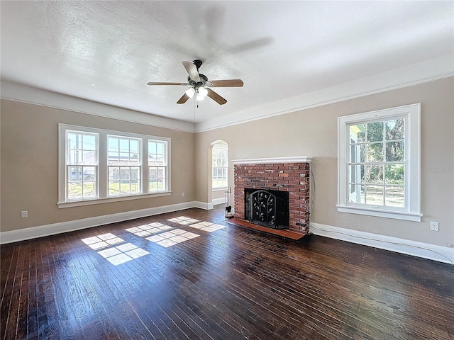 unfurnished living room featuring ceiling fan, a healthy amount of sunlight, dark wood-type flooring, and a brick fireplace