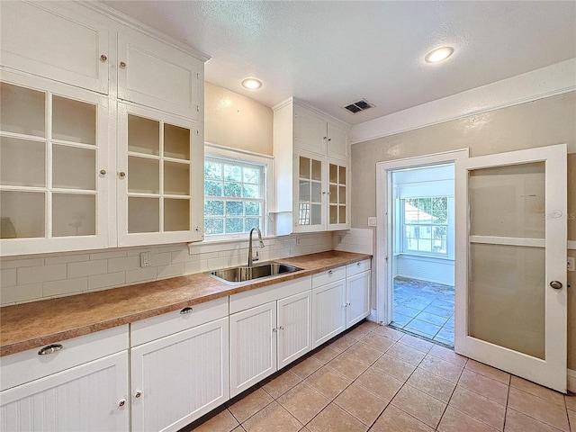 kitchen with tasteful backsplash, a textured ceiling, sink, white cabinets, and light tile patterned flooring