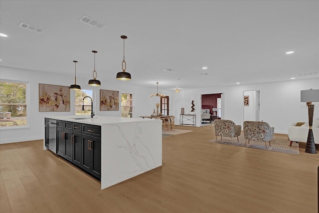 kitchen with sink, hanging light fixtures, stainless steel dishwasher, light wood-type flooring, and a large island