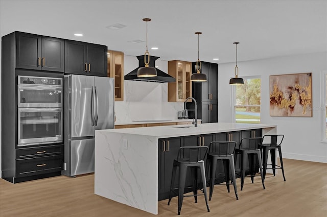 kitchen with appliances with stainless steel finishes, extractor fan, sink, pendant lighting, and a center island with sink