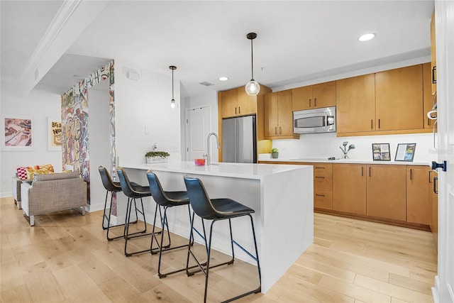 kitchen featuring stainless steel appliances, a kitchen breakfast bar, pendant lighting, light hardwood / wood-style floors, and ornamental molding