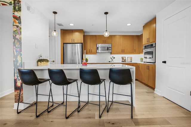 kitchen featuring a kitchen bar, appliances with stainless steel finishes, light wood-type flooring, and decorative light fixtures