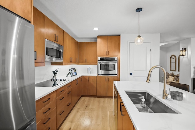 kitchen featuring decorative light fixtures, sink, appliances with stainless steel finishes, and light hardwood / wood-style flooring