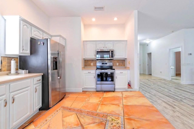 kitchen with decorative backsplash, white cabinetry, light hardwood / wood-style flooring, and appliances with stainless steel finishes