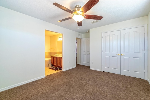 unfurnished bedroom with light carpet, ensuite bathroom, a textured ceiling, ceiling fan, and a closet