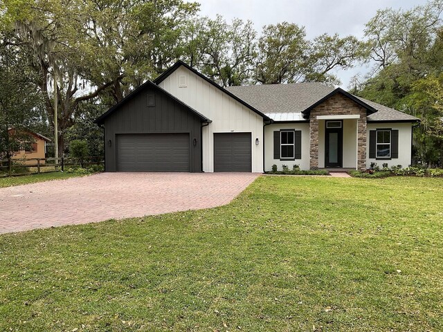 view of front facade with a front lawn, fence, roof with shingles, decorative driveway, and an attached garage