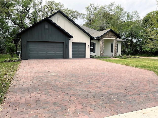 modern farmhouse featuring a front yard, a garage, stone siding, decorative driveway, and board and batten siding