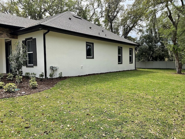 view of property exterior featuring a shingled roof, a yard, fence, and stucco siding