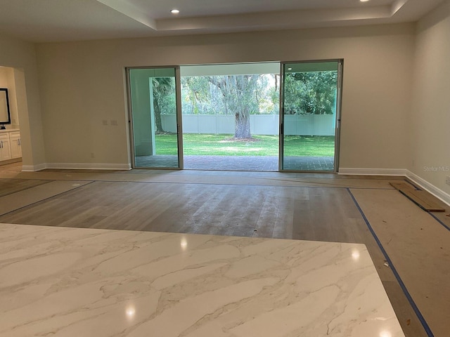 unfurnished room featuring a tray ceiling, recessed lighting, wood finished floors, and baseboards