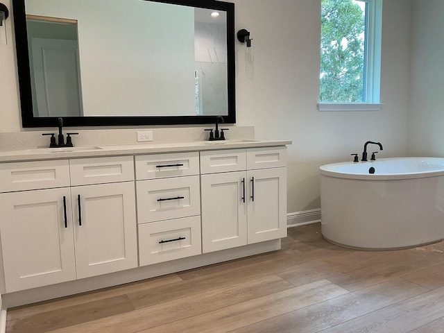 full bathroom featuring a soaking tub, wood finished floors, double vanity, and a sink