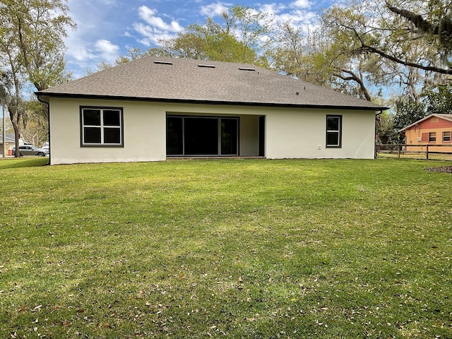 back of house featuring stucco siding, a lawn, and fence