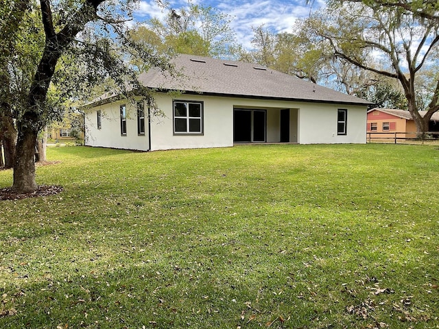 rear view of house with a lawn, fence, and stucco siding