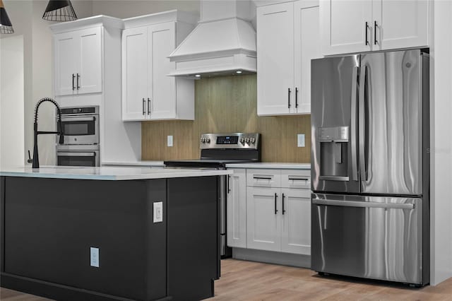 kitchen with light wood-style flooring, white cabinets, light countertops, stainless steel appliances, and custom range hood