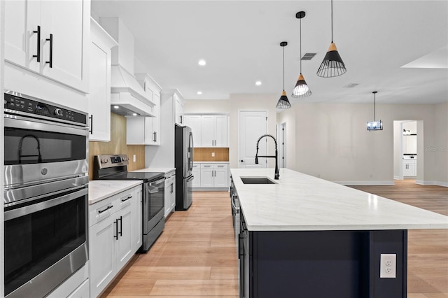 kitchen with an island with sink, light wood-style flooring, visible vents, appliances with stainless steel finishes, and custom range hood