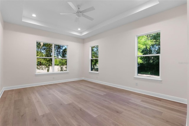 spare room with a tray ceiling, light wood-style floors, and baseboards