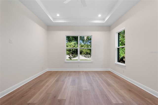 spare room featuring recessed lighting, light wood finished floors, baseboards, and a raised ceiling