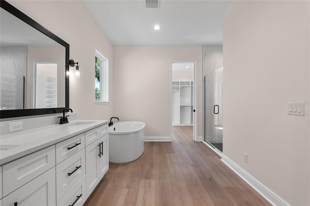 full bath with a soaking tub, a shower stall, a walk in closet, a sink, and wood finished floors
