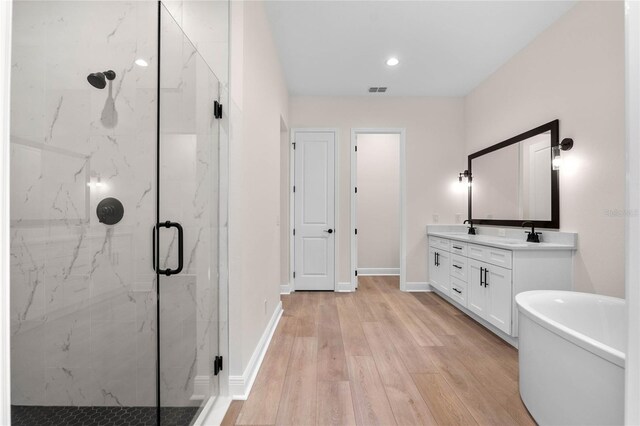 bathroom featuring baseboards, double vanity, a soaking tub, a marble finish shower, and wood finished floors