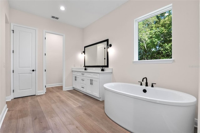 bathroom with visible vents, baseboards, a freestanding tub, double vanity, and wood finished floors