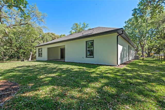 back of property with central air condition unit, stucco siding, and a lawn