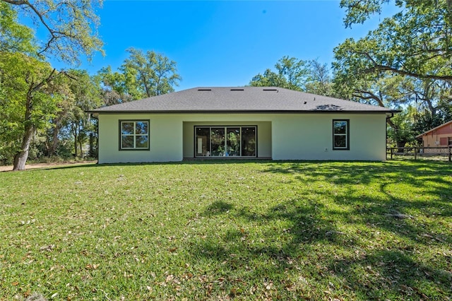 rear view of house with a yard, stucco siding, and fence