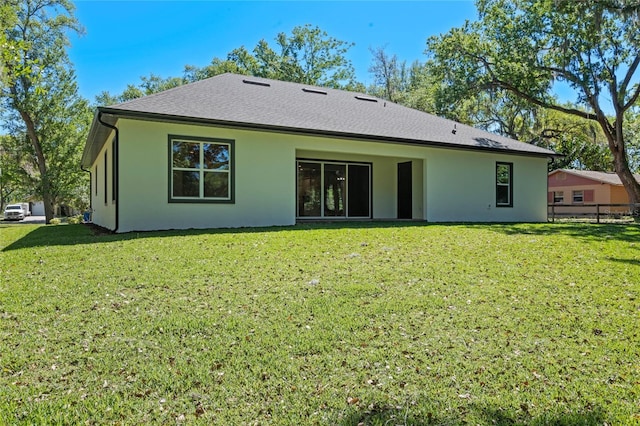 rear view of house with stucco siding, fence, and a lawn