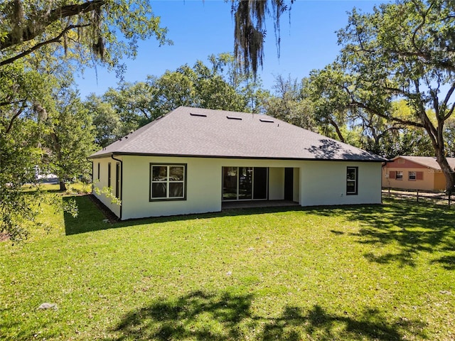rear view of house with a shingled roof, stucco siding, fence, and a lawn