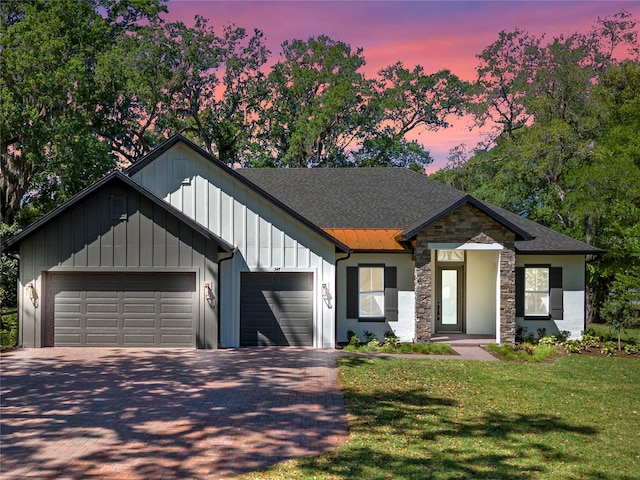 modern farmhouse featuring a front yard, stone siding, a garage, board and batten siding, and decorative driveway