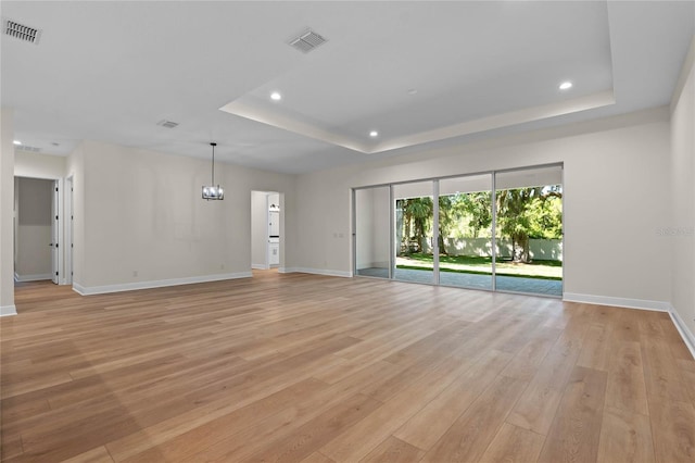 spare room featuring a tray ceiling, light wood finished floors, baseboards, and visible vents