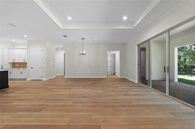 unfurnished living room with light wood-type flooring, a tray ceiling, and baseboards