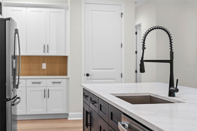 kitchen with a sink, light stone countertops, white cabinetry, and stainless steel appliances